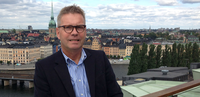 Bild på Peo Fahlström som ler in mot kameran med staden i bakgrunden