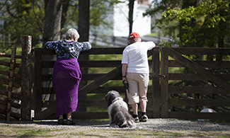 Bild på två äldre personer som lutar sig över ett staket och en hund som sitter bredvid