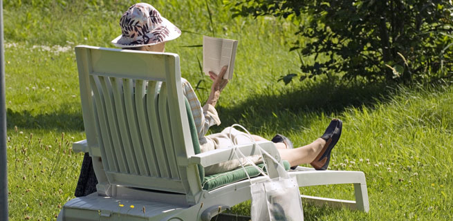 Bild på en kvinna som sitter i en solstol och läser en bok