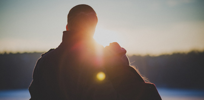 Bild på ett par som står mot solnedgången 