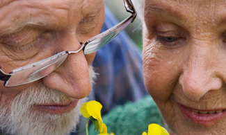 Bild på en äldre man och en äldre kvinna som luktar på blommor.