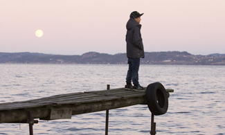 Bild på en kille som står på en brygga och kollar ut mot vattnet