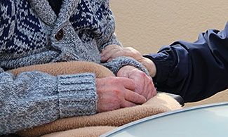 Bild på två äldre personer, ena personer håller handen om den andras arm