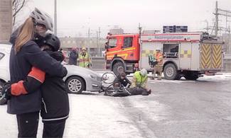 Bild på två barn som kramar om varandra och kollar på en bilolycka med brandbild och räddningstjänst i bakgrunden