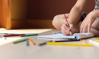 Bild på ett barn som skriver i ett skrivblock