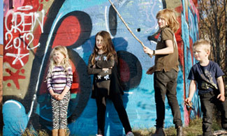 Bild på fyra barn som står framföres en graffitivägg 