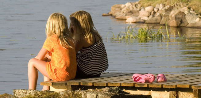 Två barn sitter och tittar ut över en sjö