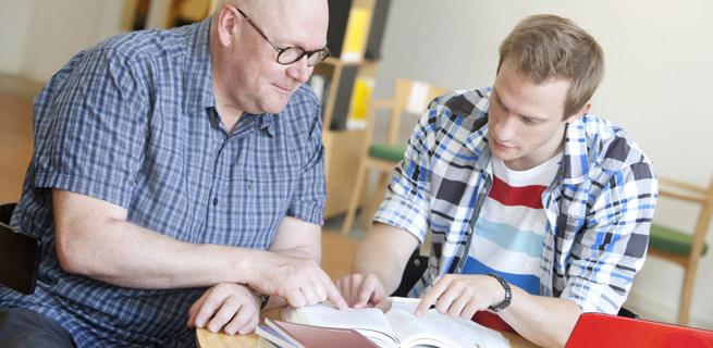 Bild på en äldre man och en yngre man som läser en bok 
