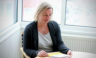 Bild på Liselott som läser avhandlingen  "Den ombokade resan – att leva som familj med kronisk sjukdom"