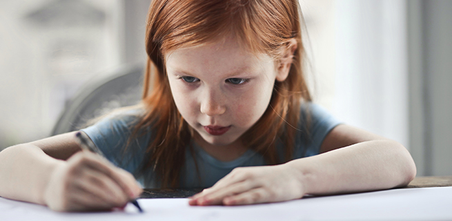Flicka håller i en penna och ritar. Foto: Pexels