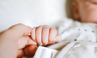Närbild på bebis som håller en vuxen i handen.