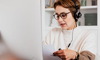 En kvinna sitter framför en datorskärm med hörlurar i öronen.