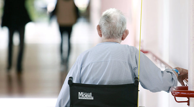 En äldre man sitter i en rullstol i en korridor.