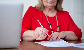 En kvinna håller i en penna och skriver på ett papper.