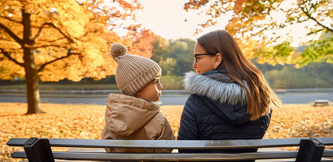 En vuxen och ett barn sitter på en parkbänk och pratar