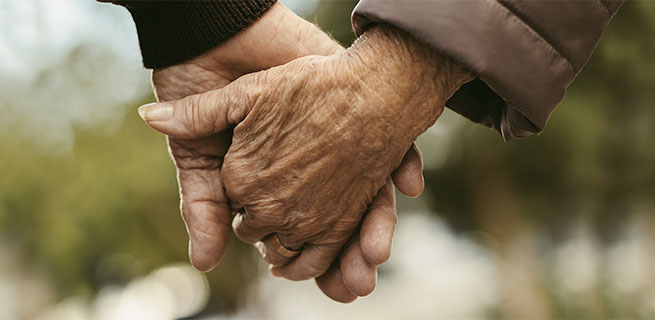 Två äldre personer håller varandra i händerna