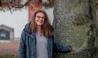 Sabina Santesson står lutad mot ett träd och tittar in i kameran.