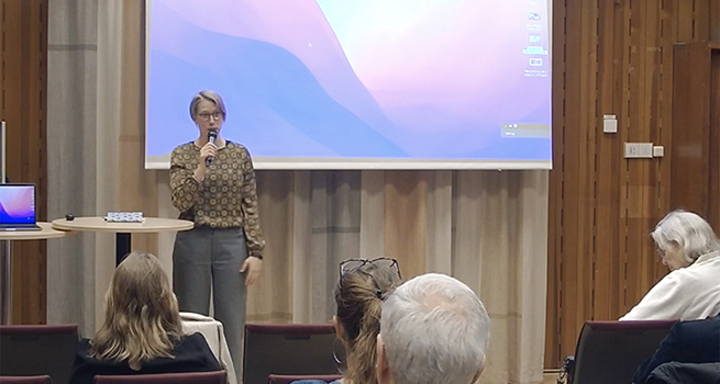 Ingrid Lindholm står framme i konferenslokalen. Bakom hennes syns en skärm.