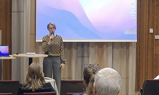 Ingrid Lindholm står framme i konferenslokalen. Bakom hennes syns en skärm.