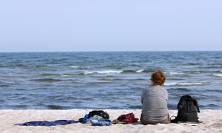 En person sitter på stranden och tittar ut mot havet