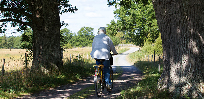 Äldre dam som cyklar på en grusväg